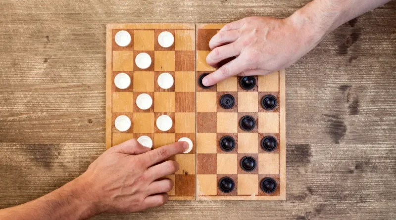 Duas pessoas jogando damas. Mãos movendo peças no tabuleiro.