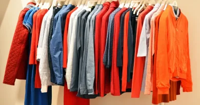 Roupas masculinas e femininas variadas em cabides, incluindo camisas, blusas e jaquetas de diversas cores como azul, vermelho e cinza.