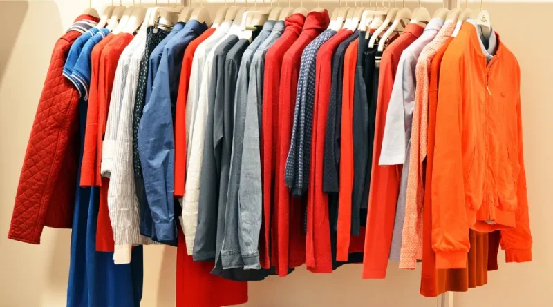 Roupas masculinas e femininas variadas em cabides, incluindo camisas, blusas e jaquetas de diversas cores como azul, vermelho e cinza.