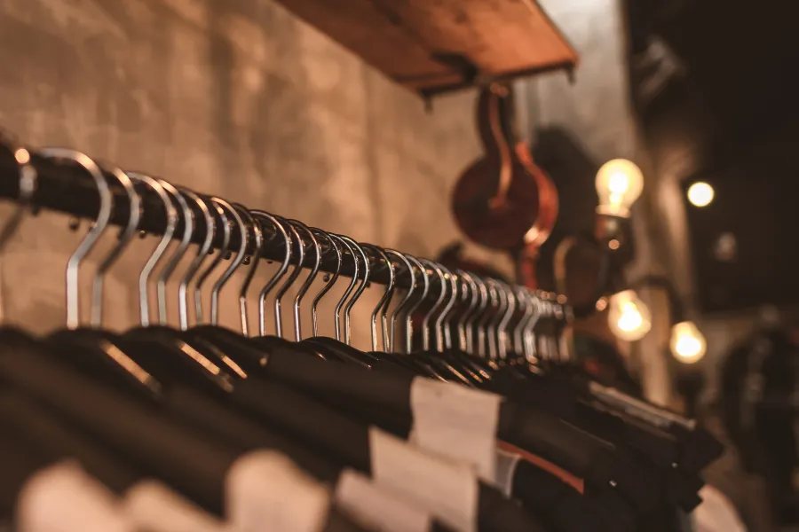 Cabides de metal vazios em uma arara, com iluminação quente de lâmpadas vintage em um ambiente de loja rústica, sugerindo atmosfera de boutique de moda.