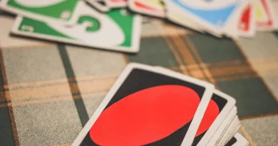 Uma mão segurando cartas de Uno coloridas com números e símbolos, sobre um fundo desfocado.