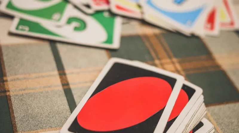 Uma mão segurando cartas de Uno coloridas com números e símbolos, sobre um fundo desfocado.