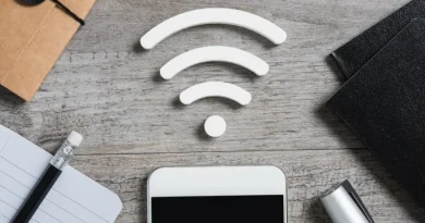 Imagem de um smartphone com um ícone branco de Wi-Fi acima, sobre uma mesa de madeira com objetos como um caderno, lápis e caneta.