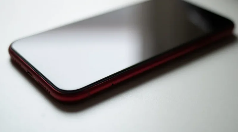 Close-up lateral de um celular smartphone vermelho deitado sobre uma superfície branca