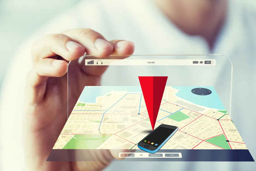 Mão segurando um dispositivo transparente com mapa e um pino de localização vermelho apontando para um celular